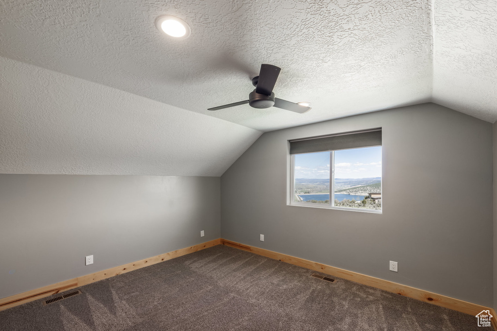 Bonus room featuring baseboards, vaulted ceiling, ceiling fan, a textured ceiling, and dark colored carpet