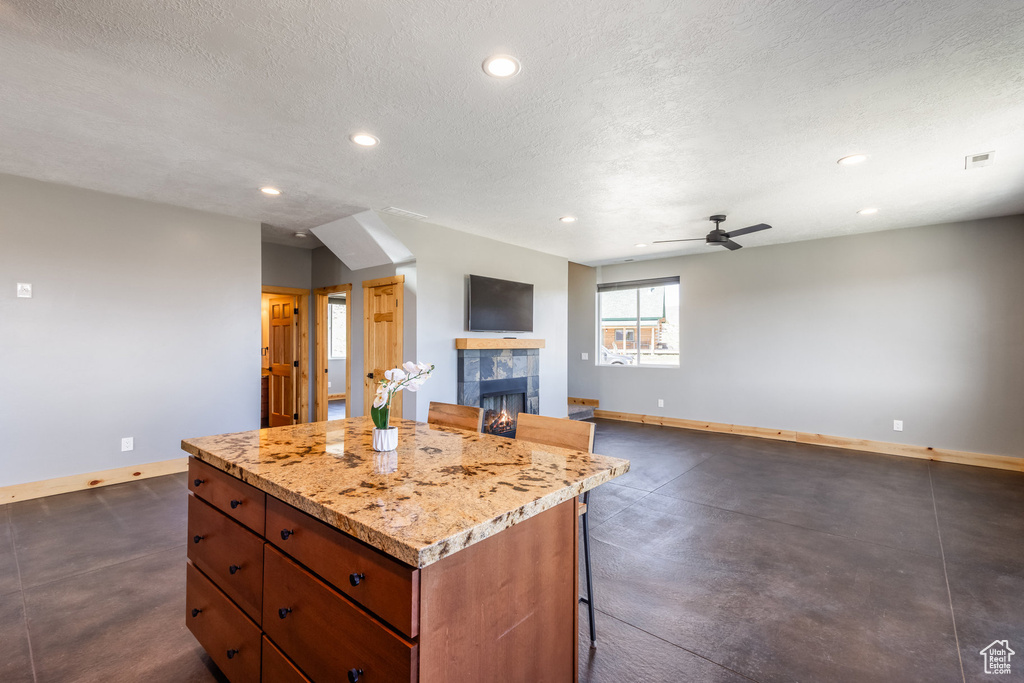 Kitchen featuring baseboards, a tiled fireplace, a center island, recessed lighting, and a breakfast bar
