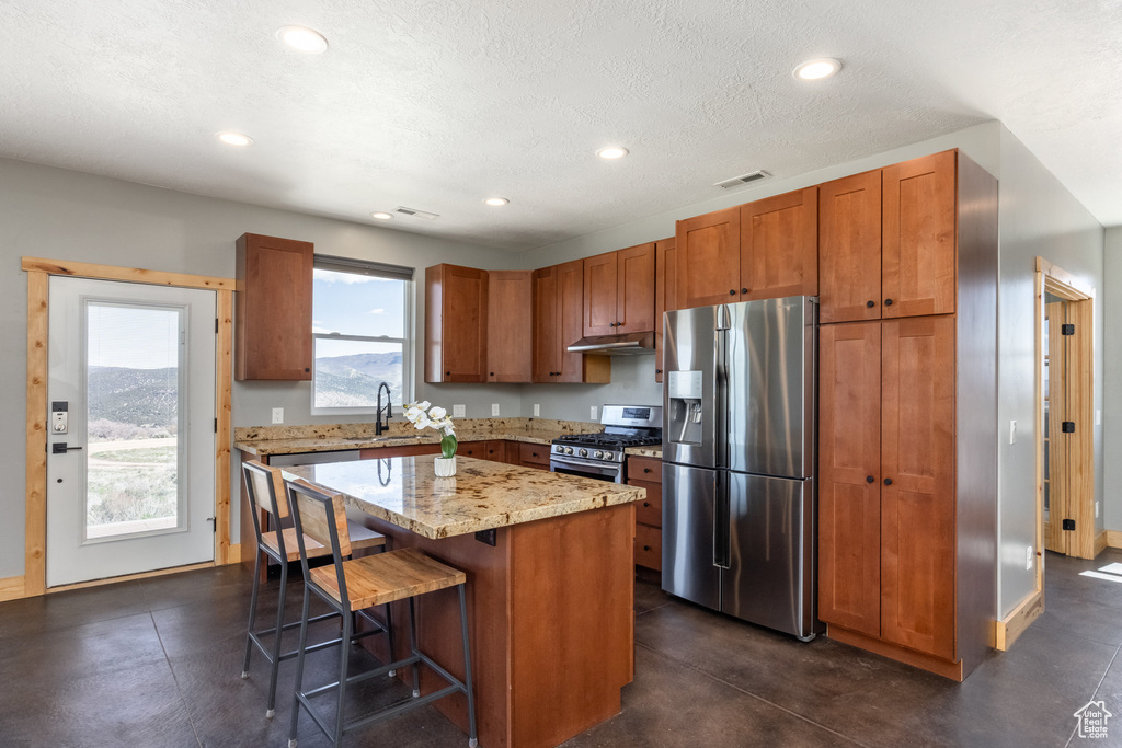 Kitchen with appliances with stainless steel finishes, under cabinet range hood, a kitchen breakfast bar, recessed lighting, and a kitchen island
