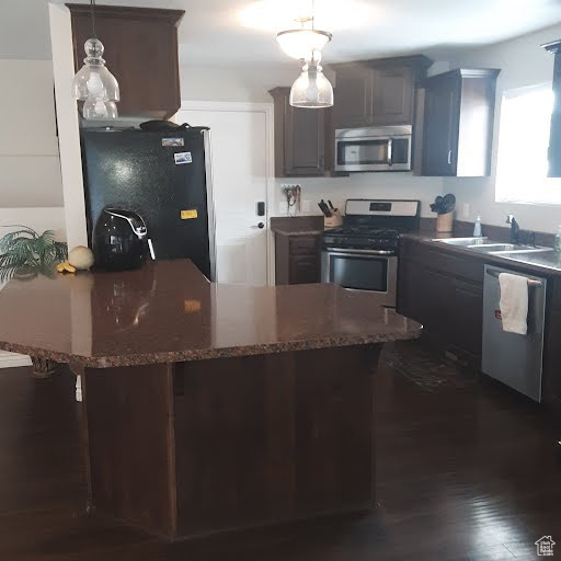 Kitchen featuring stainless steel appliances, a sink, decorative light fixtures, dark stone counters, and a kitchen breakfast bar