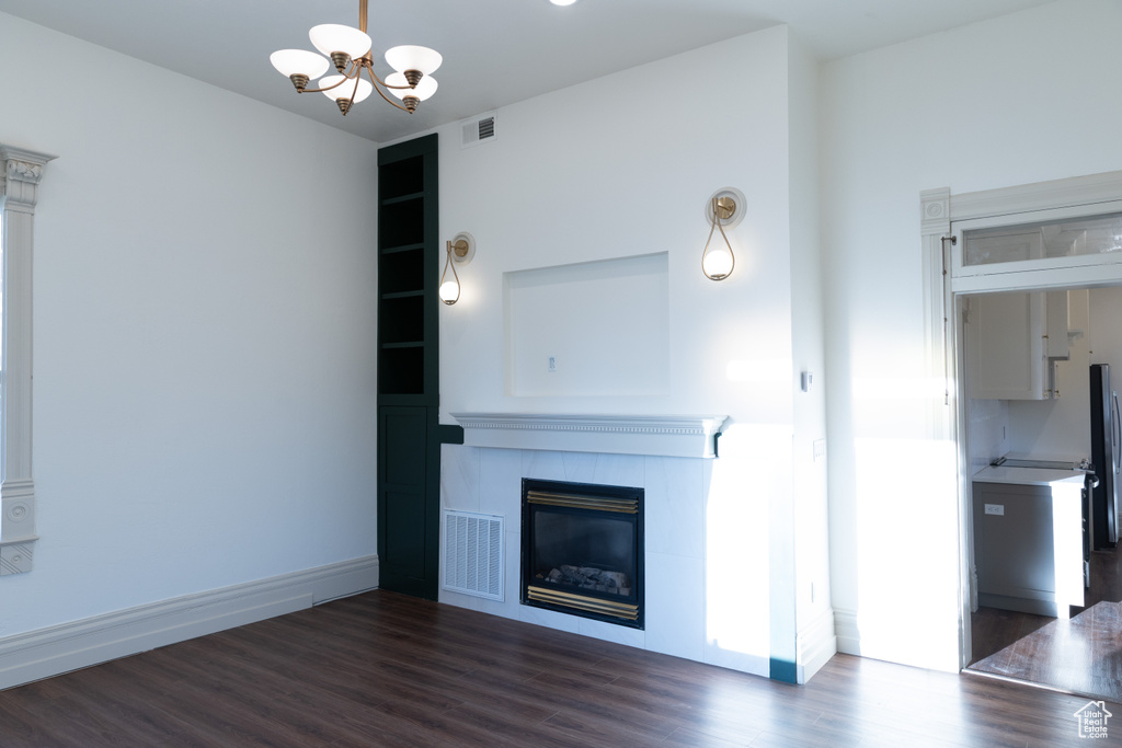 Unfurnished living room with a chandelier, dark wood-style floors, a tiled fireplace, and baseboards