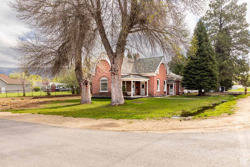 View of front of property with brick siding, a porch, a shingled roof, and a chimney