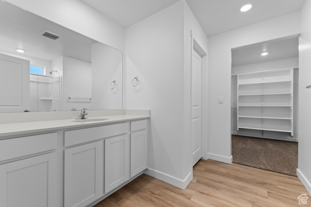 Bathroom featuring baseboards, vanity, recessed lighting, wood finished floors, and a shower