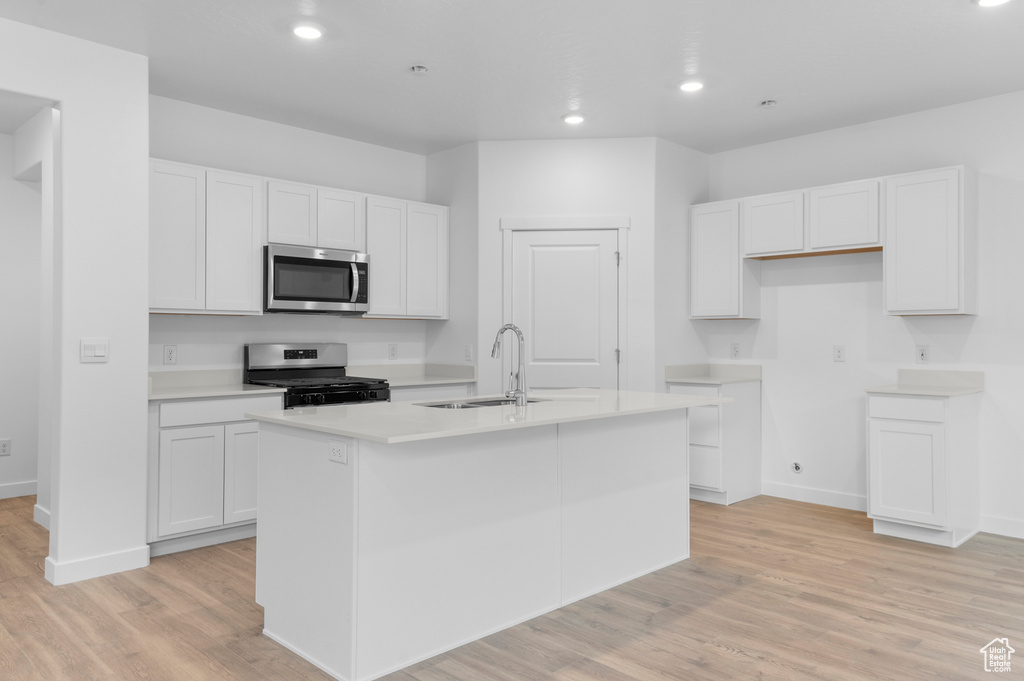 Kitchen with appliances with stainless steel finishes, a sink, recessed lighting, an island with sink, and white cabinetry