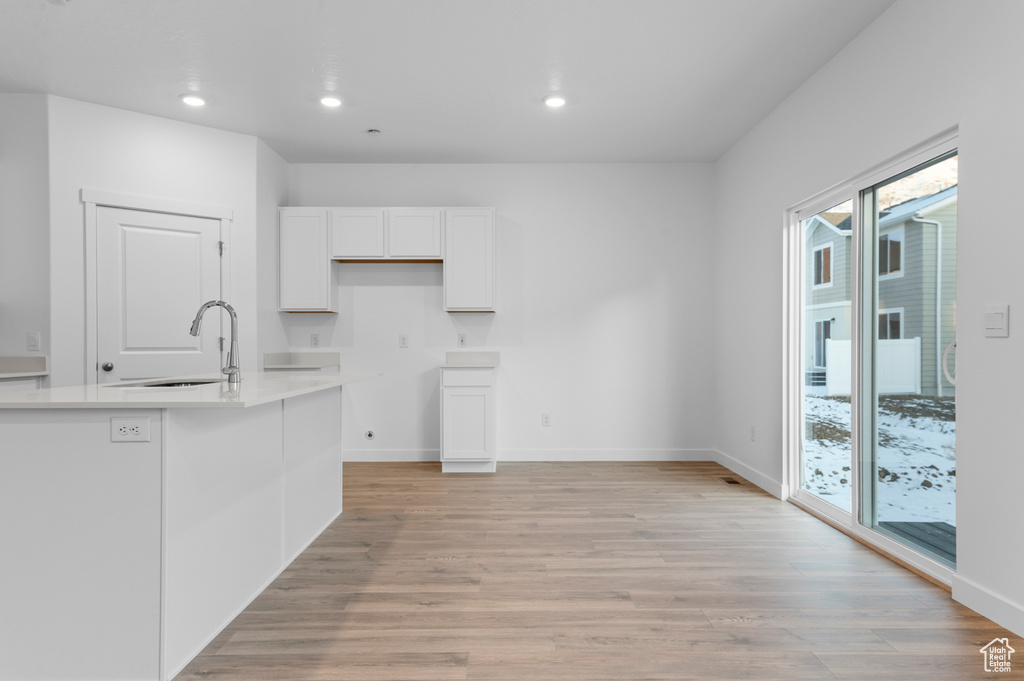 Kitchen featuring a sink, white cabinets, recessed lighting, light wood-style floors, and baseboards