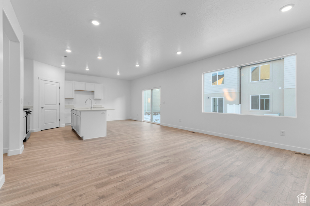 Unfurnished living room featuring a sink, light wood-type flooring, recessed lighting, and baseboards