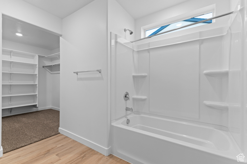 Full bath with wood finished floors, bathing tub / shower combination, baseboards, and a walk in closet