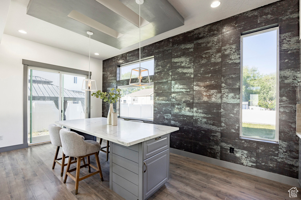 Kitchen with gray cabinets, dark wood-style flooring, tile walls, a kitchen island, and light stone countertops