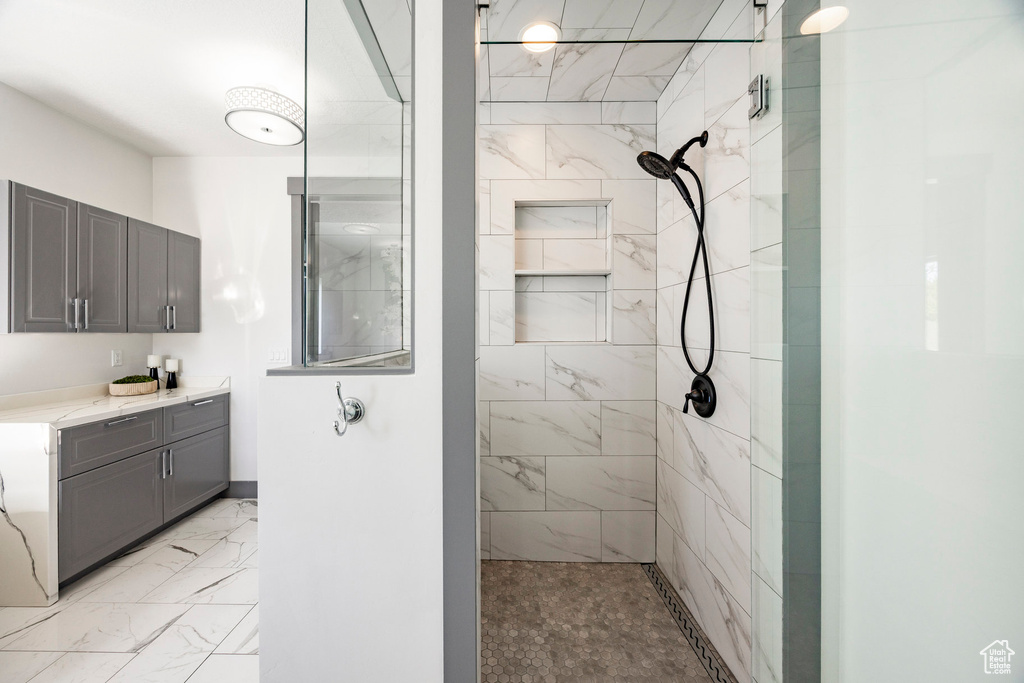 Full bathroom featuring tiled shower, vanity, and marble finish flooring