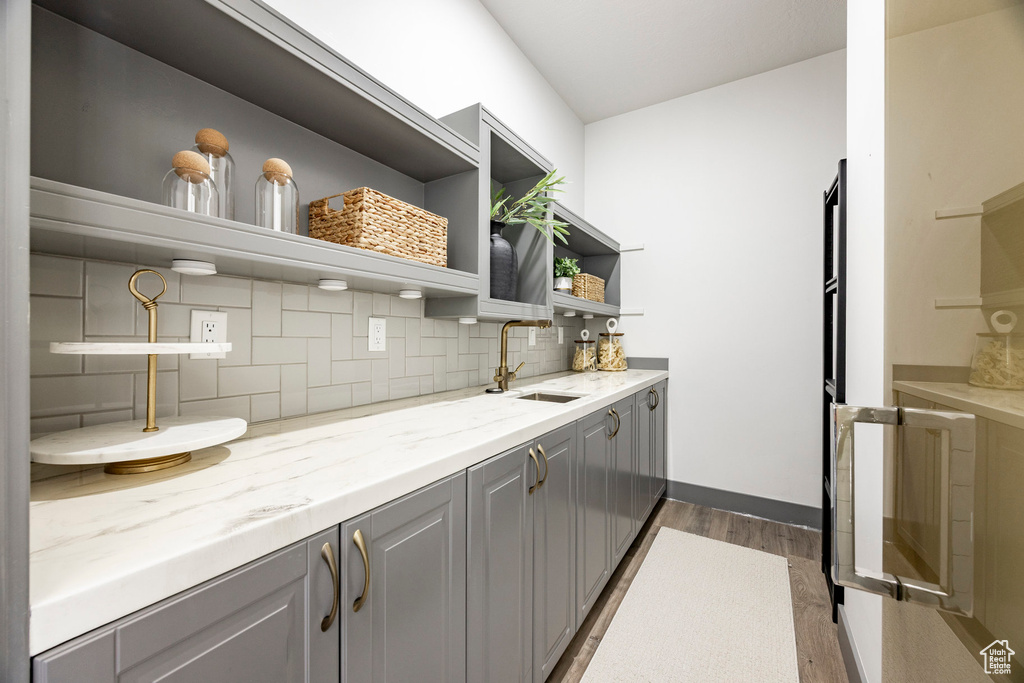 Kitchen featuring open shelves, gray cabinetry, dark wood-type flooring, backsplash, and light stone counters