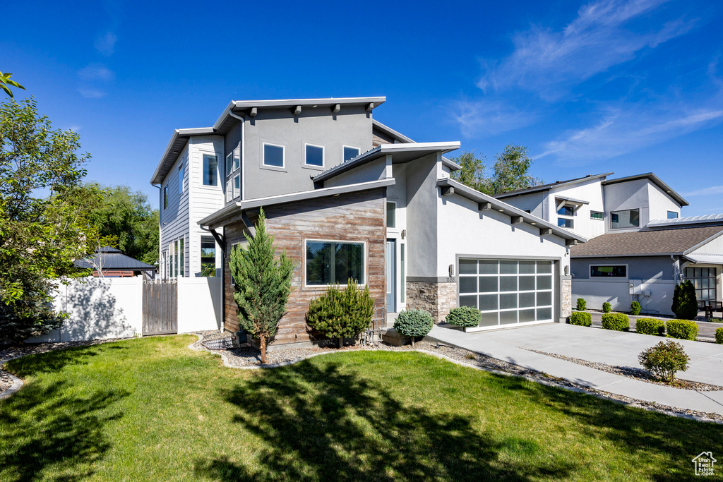 View of front facade featuring driveway, stone siding, stucco siding, and an attached garage
