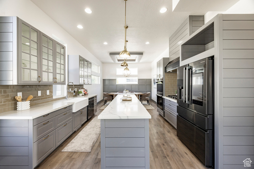 Kitchen featuring gray cabinets, a sink, a kitchen island, double wall oven, and glass insert cabinets