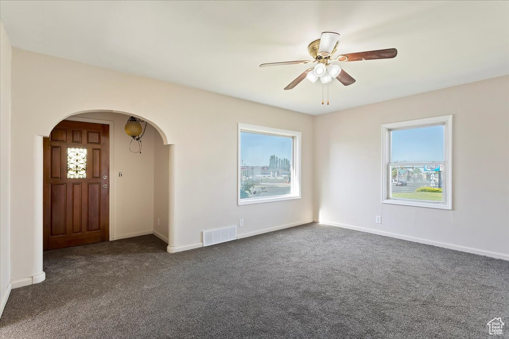 Unfurnished room featuring arched walkways, dark carpet, a ceiling fan, and baseboards