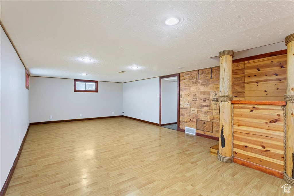 Below grade area with light wood-type flooring, a textured ceiling, baseboards, and recessed lighting