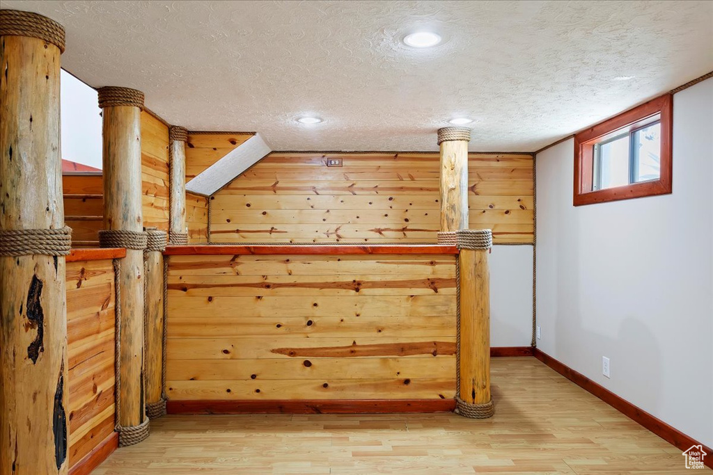 Below grade area with light wood-style flooring, a textured ceiling, baseboards, and recessed lighting