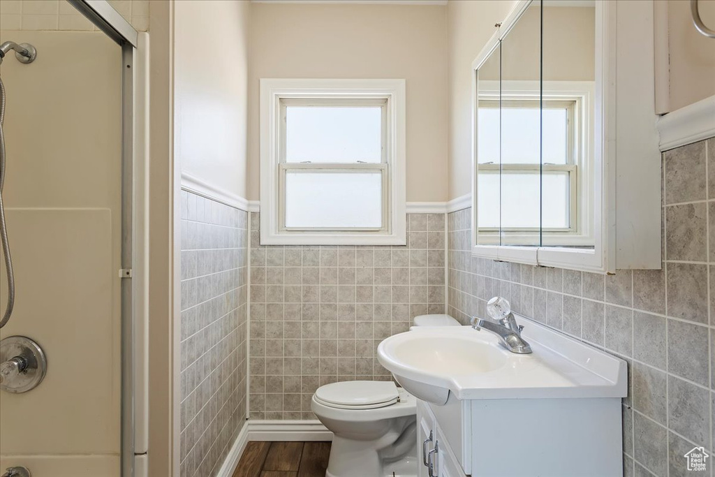 Full bath featuring tile walls, a shower with door, vanity, wood finished floors, and toilet