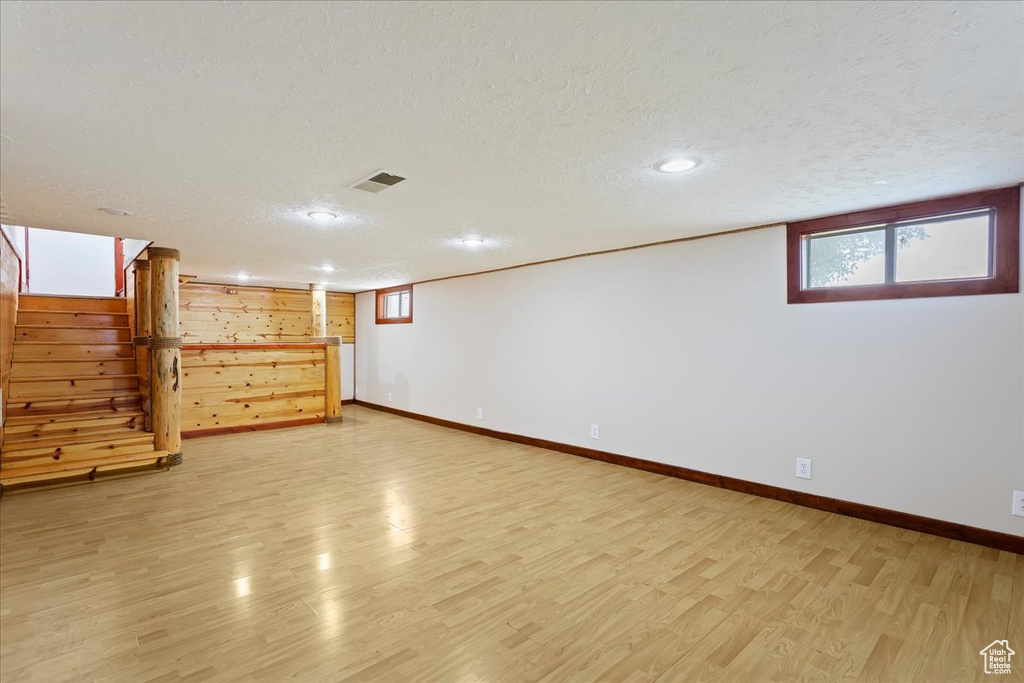 Basement featuring a textured ceiling, light wood-type flooring, baseboards, stairs, and recessed lighting