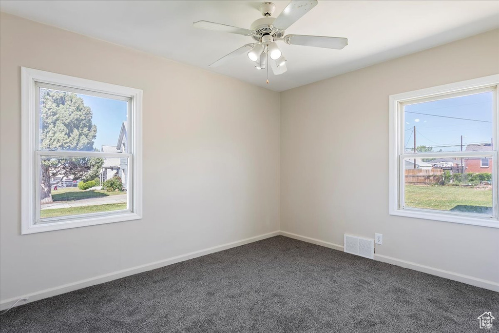 Empty room with dark carpet, plenty of natural light, baseboards, and a ceiling fan