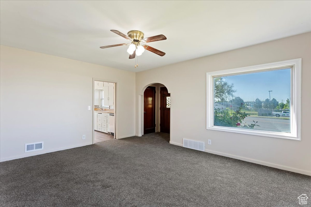 Carpeted empty room featuring arched walkways, ceiling fan, and baseboards