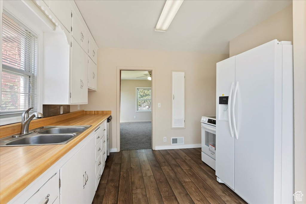 Kitchen featuring white appliances, a sink, white cabinets, and dark wood-type flooring