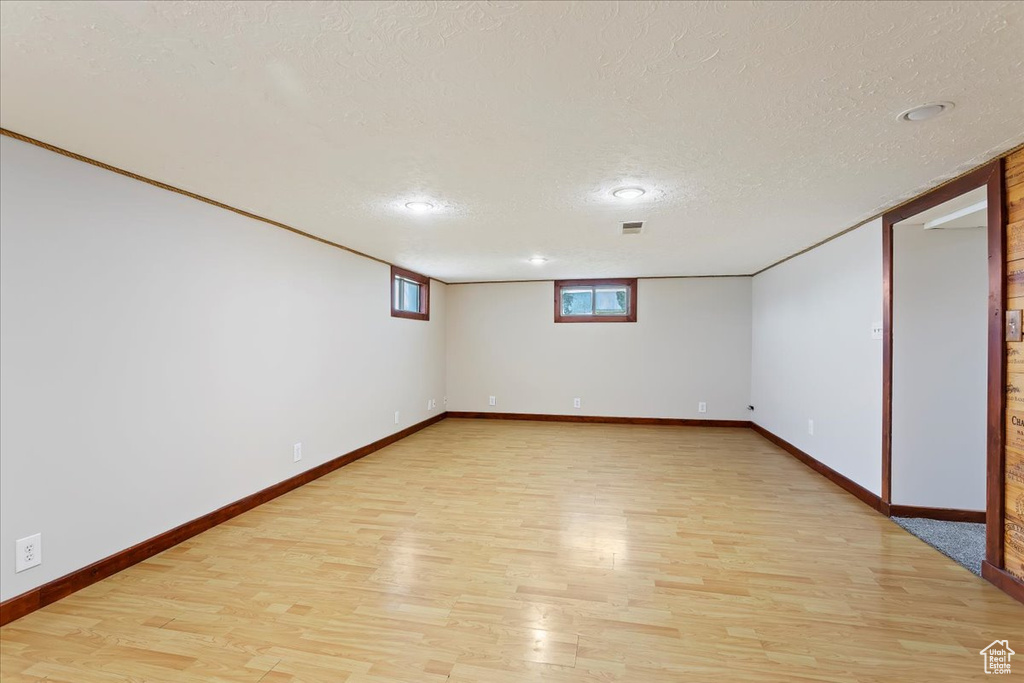 Below grade area with light wood finished floors, a textured ceiling, baseboards, and recessed lighting