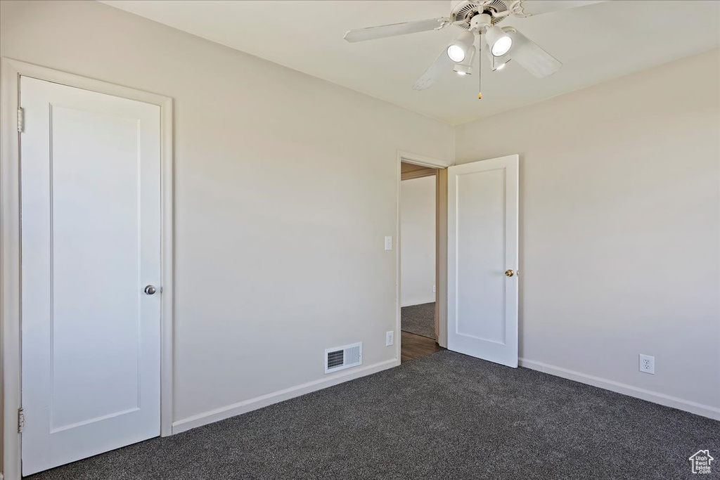 Unfurnished bedroom featuring dark carpet, baseboards, and a ceiling fan