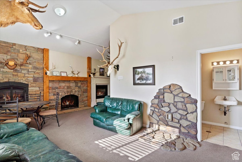 Carpeted living area with a stone fireplace, vaulted ceiling, a sink, tile patterned floors, and baseboards