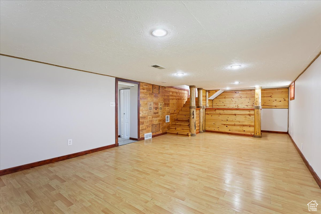 Finished basement with light wood-style flooring, baseboards, a textured ceiling, wood walls, and stairway