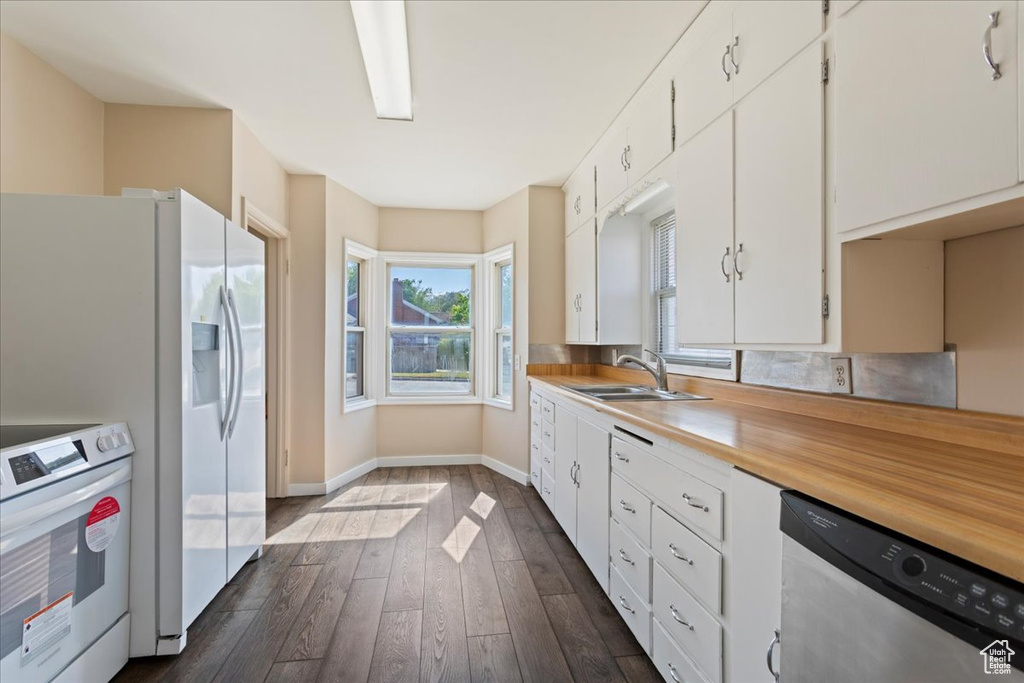 Kitchen featuring white appliances, a sink, white cabinetry, light countertops, and dark wood finished floors