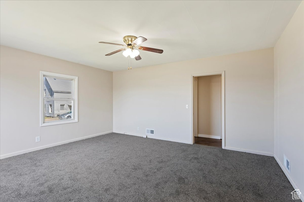 Empty room with dark carpet, a ceiling fan, and baseboards