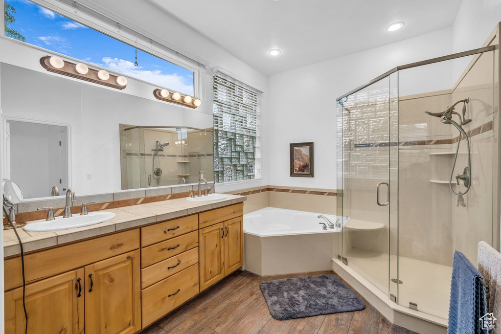 Full bathroom with a shower stall, a bath, double vanity, and wood finished floors