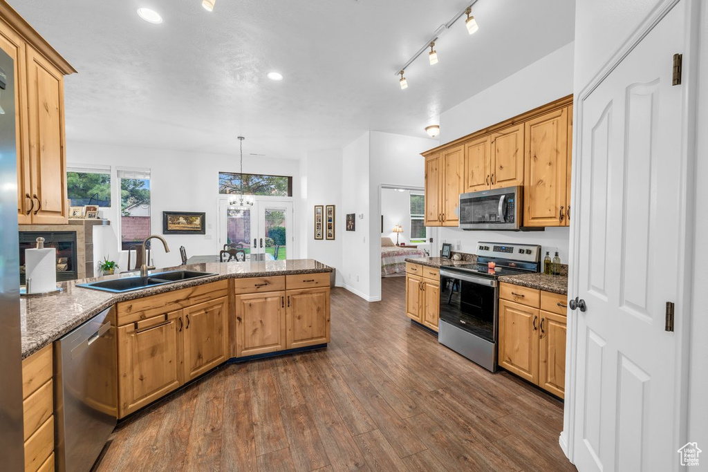 Kitchen featuring stainless steel appliances, a sink, a peninsula, dark wood-style floors, and dark stone counters