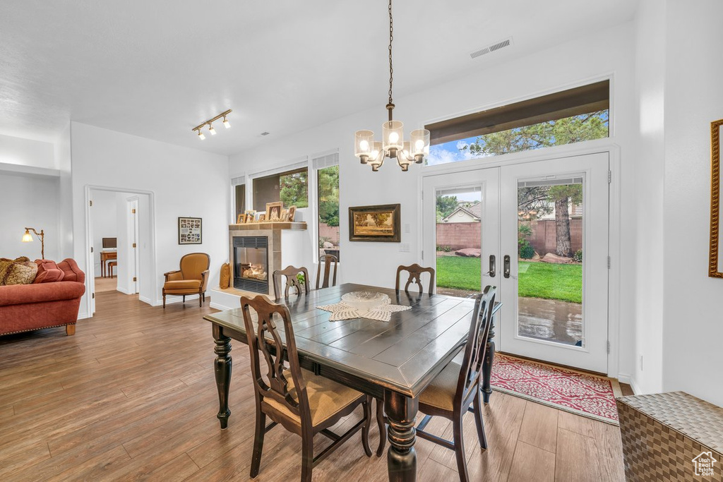 Dining space with a tiled fireplace, a chandelier, wood finished floors, and french doors