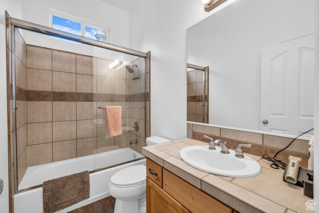 Full bath featuring toilet, shower / bath combination with glass door, vanity, and wood finished floors