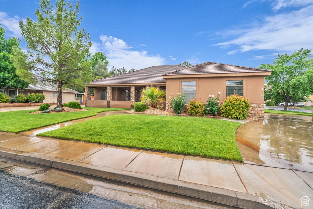 Ranch-style house with stucco siding, a front yard, a tiled roof, and stone siding