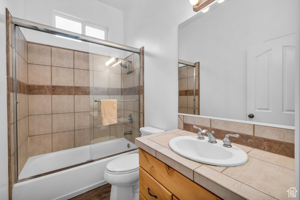 Bathroom with toilet, vanity, and combined bath / shower with glass door