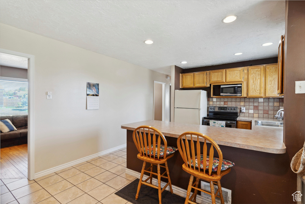 Kitchen with appliances with stainless steel finishes, a sink, baseboards, a peninsula, and light countertops