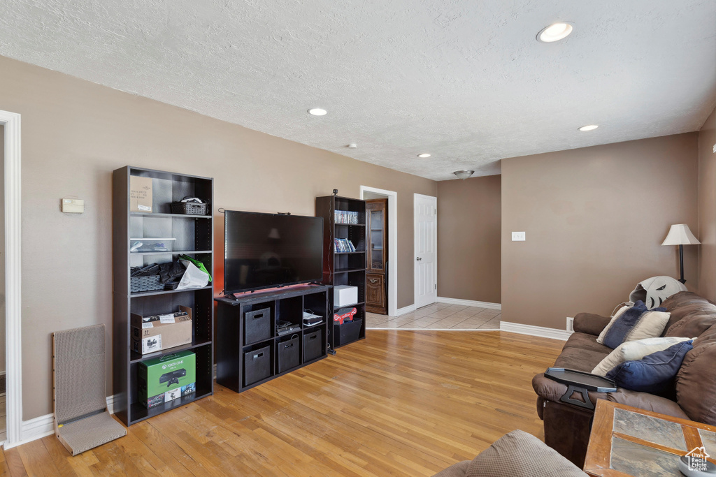 Living area with light wood-style floors, baseboards, recessed lighting, and a textured ceiling