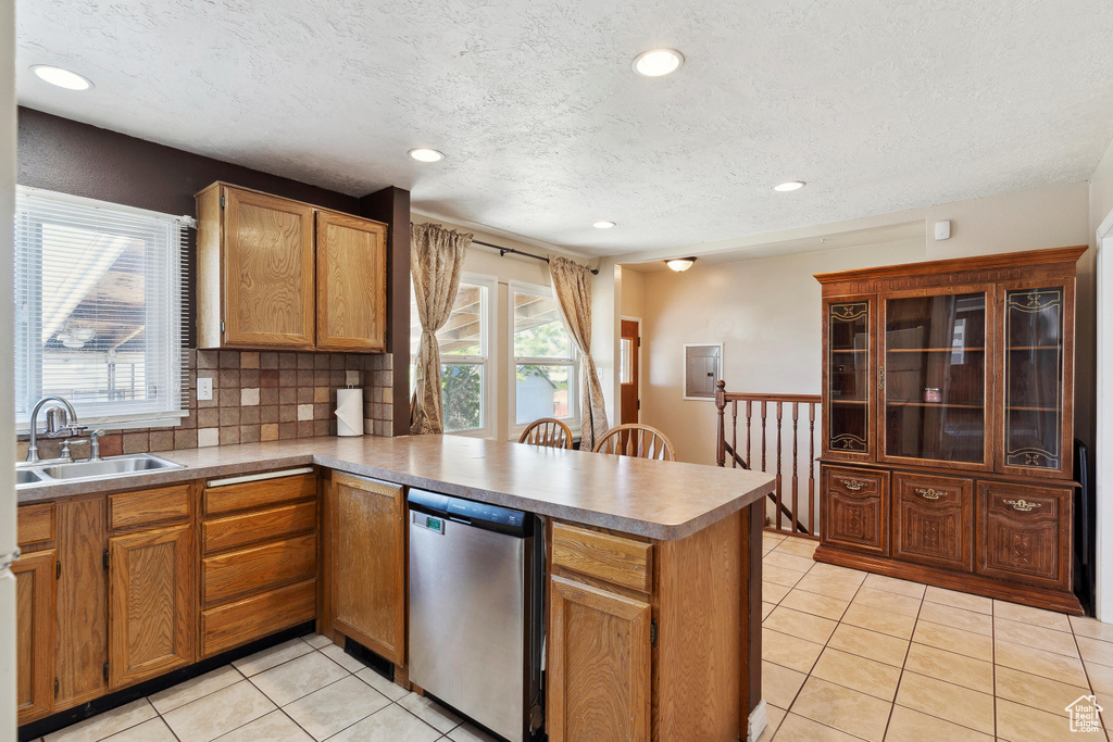 Kitchen with stainless steel dishwasher, a sink, a peninsula, light tile patterned floors, and a textured ceiling