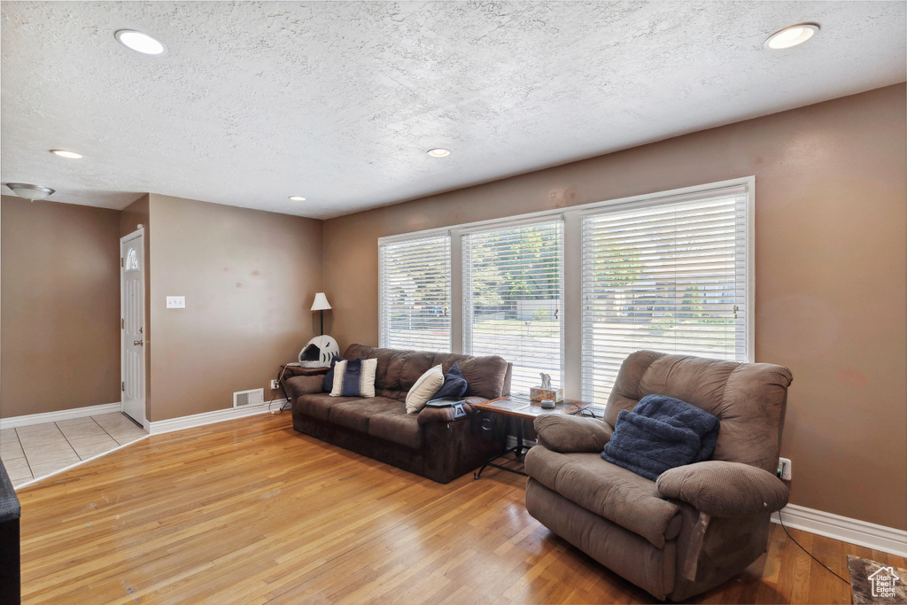 Living room with a textured ceiling, light wood-type flooring, recessed lighting, and baseboards
