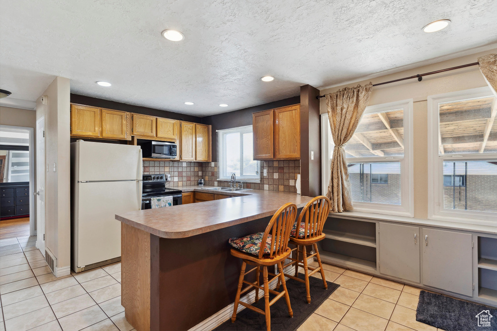 Kitchen with appliances with stainless steel finishes, light tile patterned floors, a peninsula, backsplash, and recessed lighting