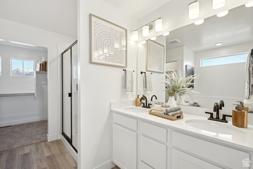 Bathroom with wood finished floors, a shower stall, double vanity, and baseboards