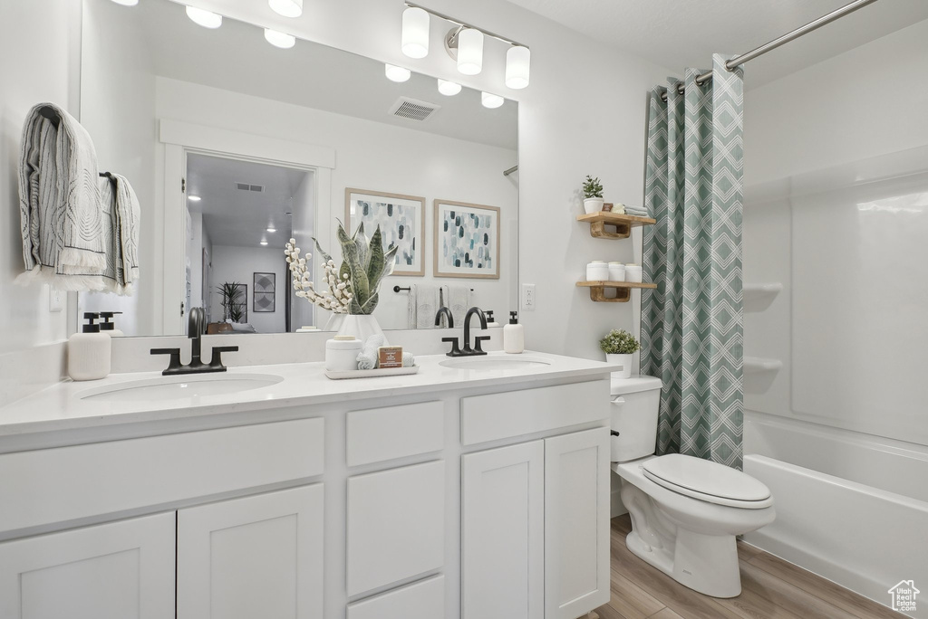 Full bathroom with toilet, double vanity, wood finished floors, and shower / bath combo with shower curtain