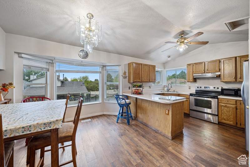 Kitchen featuring stainless steel appliances, a peninsula, brown cabinets, under cabinet range hood, and vaulted ceiling