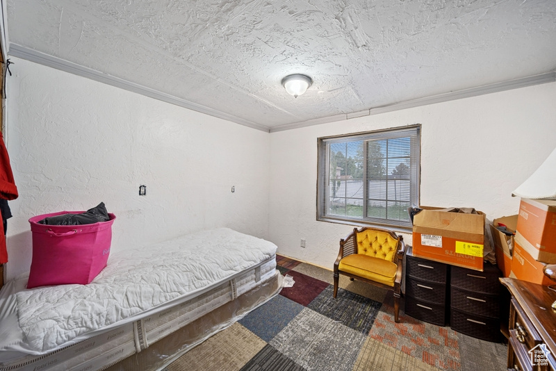 Bedroom with a textured ceiling, ornamental molding, and a textured wall