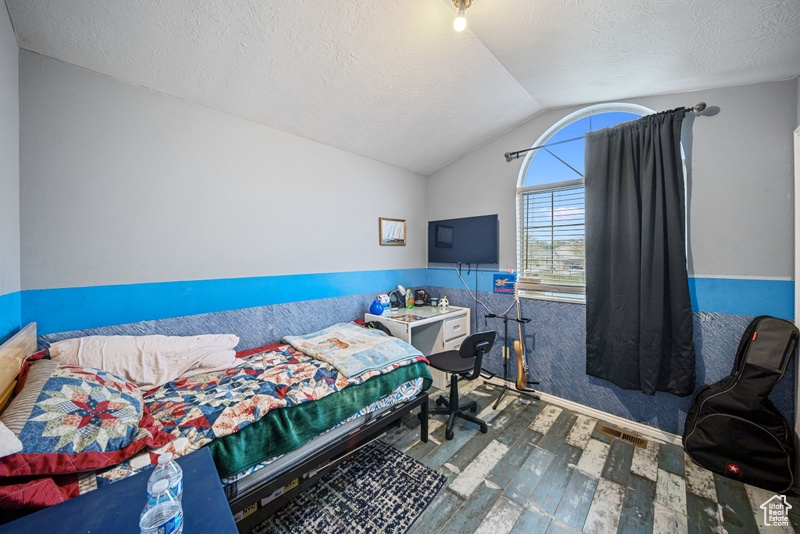 Bedroom with hardwood / wood-style floors, lofted ceiling, and a textured ceiling