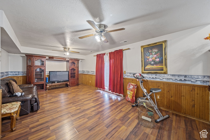 Living room featuring a wainscoted wall, wooden walls, wood finished floors, a ceiling fan, and a textured ceiling