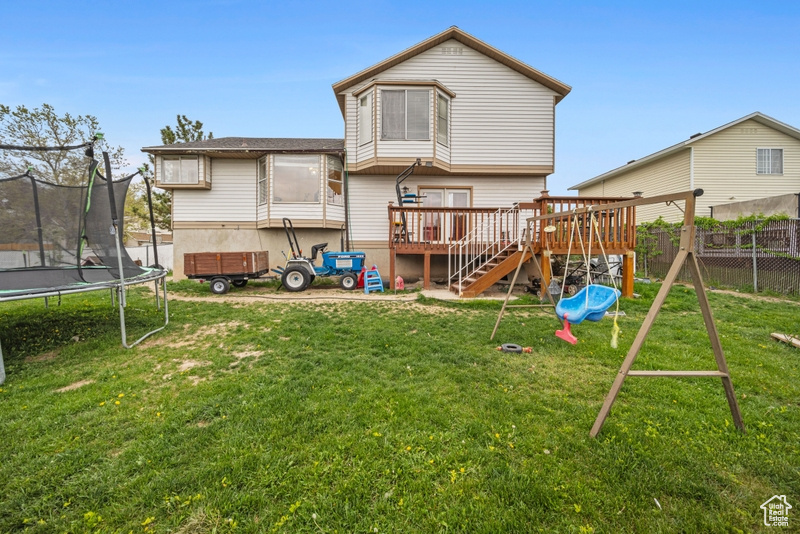 Back of property featuring a trampoline, a wooden deck, a playground, and stairway