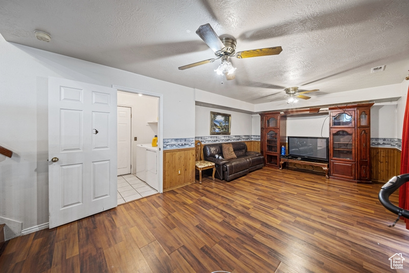 Living room with wood finished floors, a textured ceiling, a ceiling fan, and a wainscoted wall