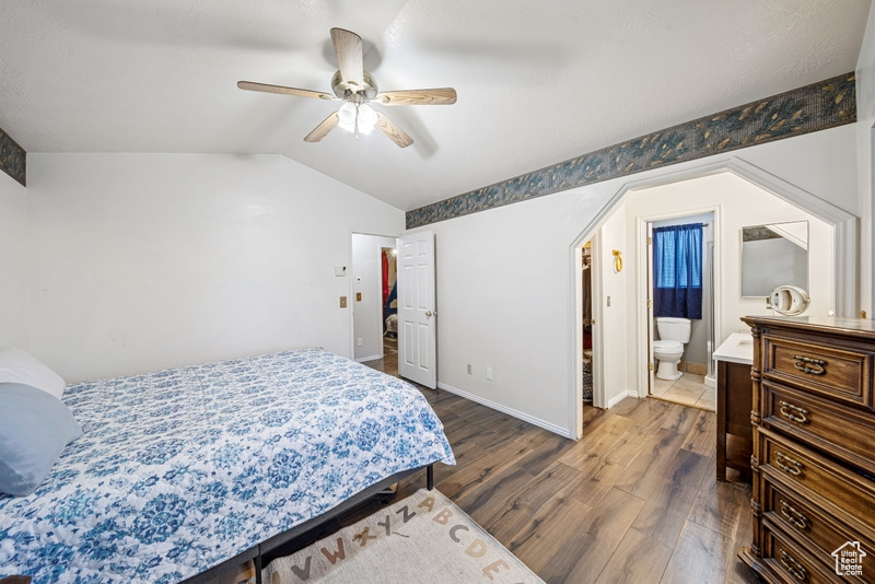Bedroom with dark wood finished floors, vaulted ceiling, baseboards, ceiling fan, and ensuite bath